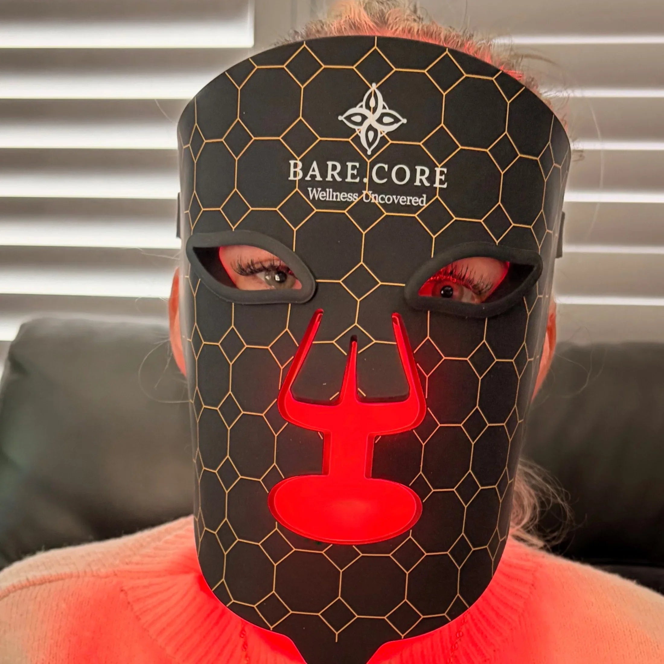 Person wearing black LED light therapy mask with honeycomb pattern for skincare